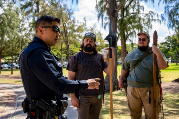 Andrew Roberts, center, director of the Hawaii Firearms Coalition, holds a halberd while talking to a Honolulu police officer at Kapiolani Park on Saturday, June 22, 2024, in Honolulu, Hawaii.